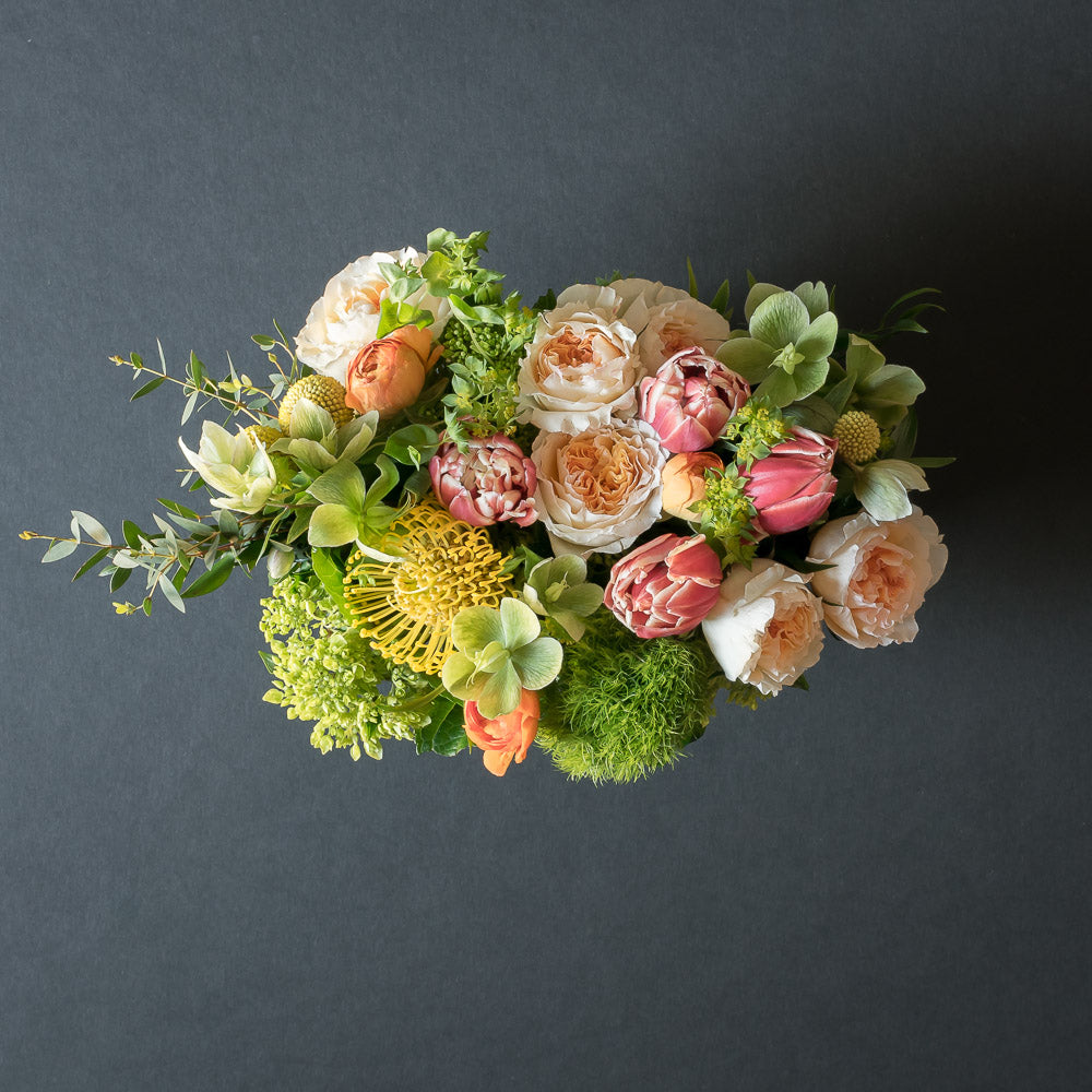 From the top: beautiful floral arrangement with blush roses, red tulips, hellebores, hydrangeas, and yellow balls