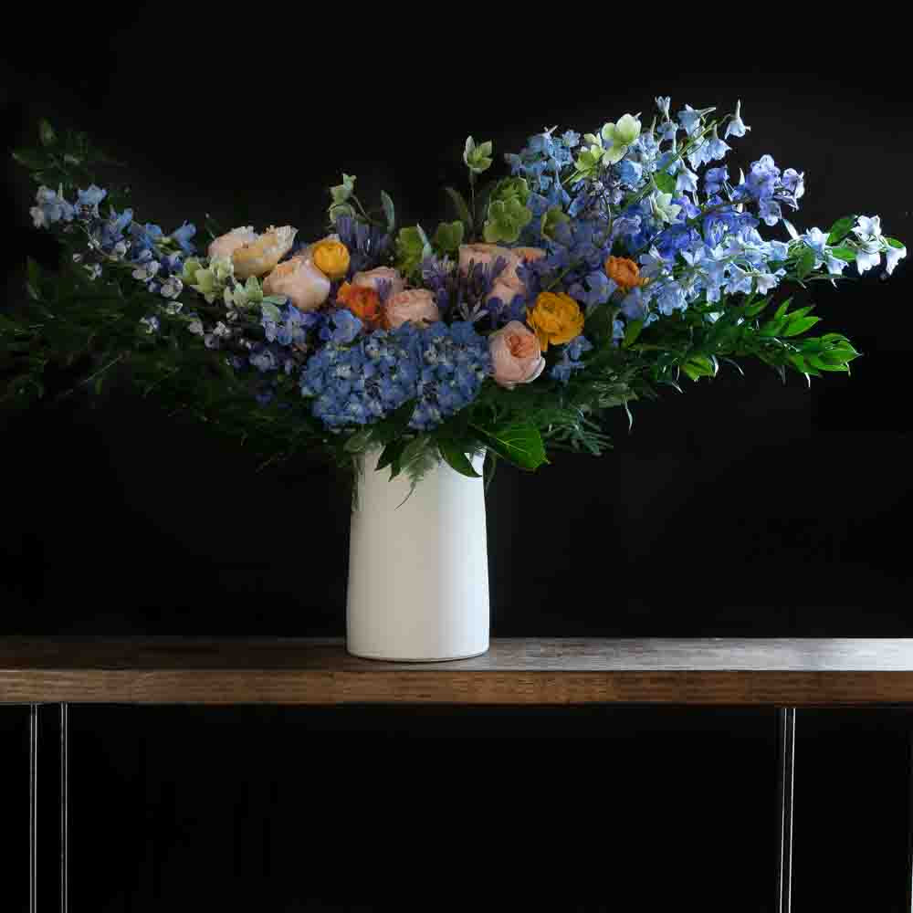 Boutique tall floral arrangement with blush roses, blue flowers, hellebores, hydrangeas