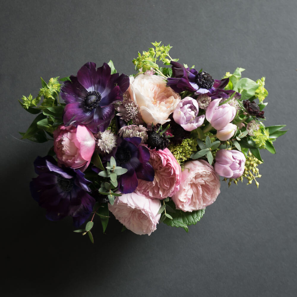 Unique floral arrangement with light pink David Austin garden roses, light pink small roses, purple anemonies, and mini green hydrangeas, from the top