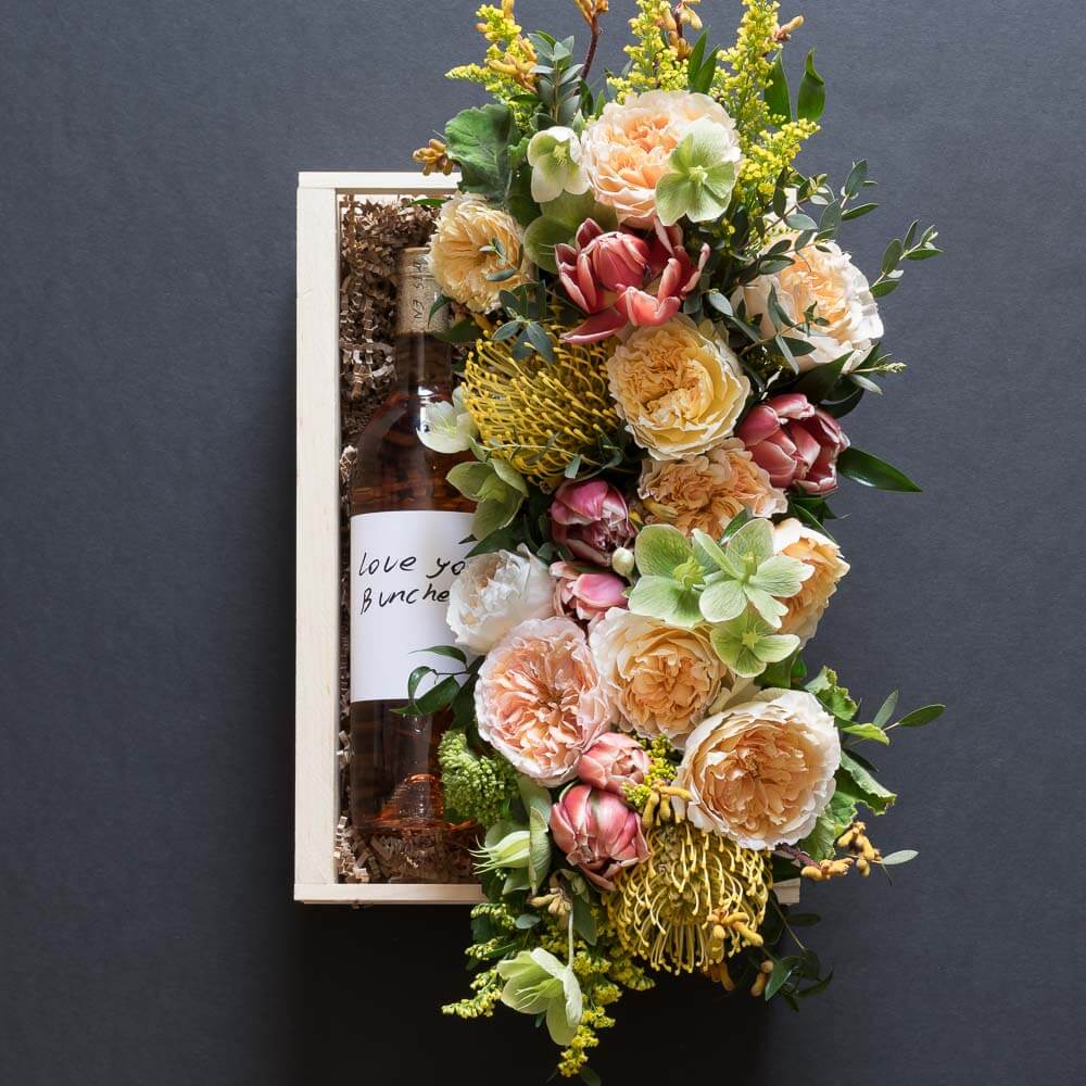 Beautiful floral gift box with blush roses, red tulips, hellebores, hydrangeas, and yellow balls, with organic rose wine