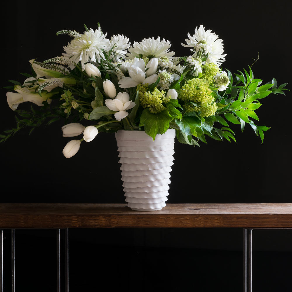 Tall boutique floral arrangement with white tulips, white roses, white calla lilies, and green mini hydrangeas