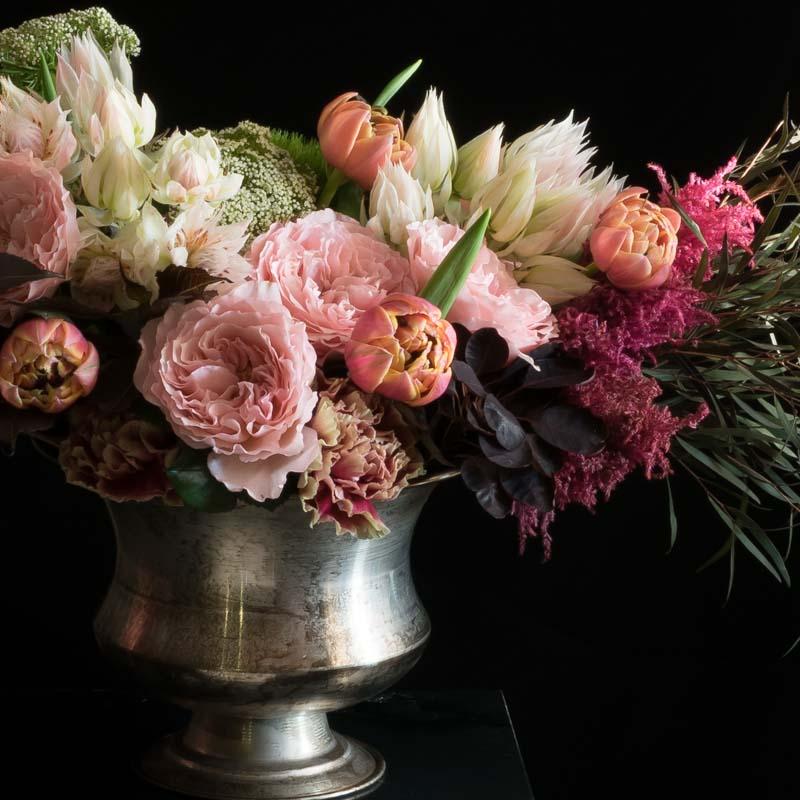 Boutique floral arrangement with pink fragrant garden roses, burgundy flowers, pink, orange tulips, and white flowers.