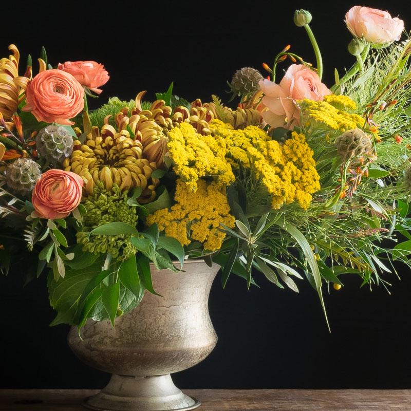 Beatiful boutique fall floral arrangement with orange, yellow flowers, and light orange ranunculus.