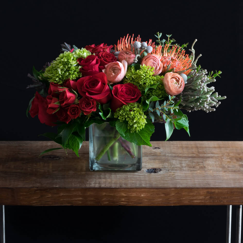 Boutique unique floral arrangement using the best flowers - red roses, peach ranunculus, mini hydrangeas, and proteas.