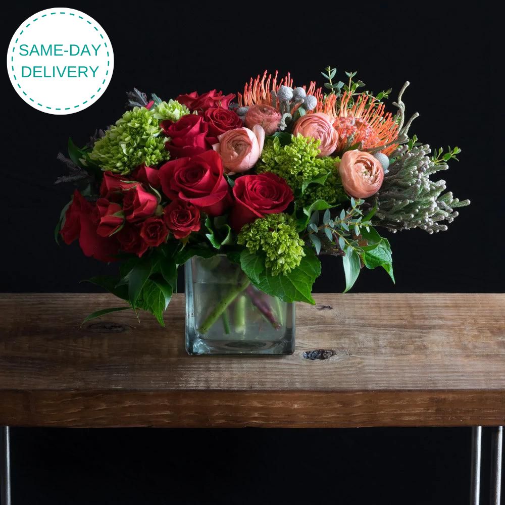 Boutique unique floral arrangement using the best flowers - red roses, peach ranunculus, mini hydrangeas, and proteas.