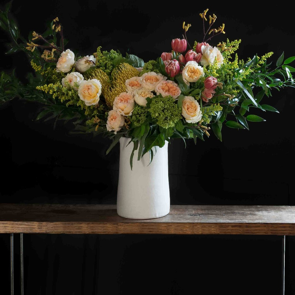 Boutique tall floral arrangement with blush roses, red tulips, hellebores, hydrangeas, and yellow balls