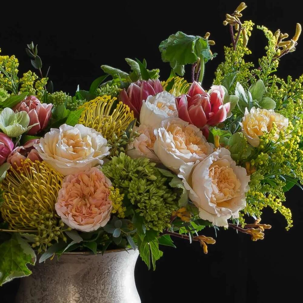 Boutique Luxe floral arrangement with blush roses, red tulips, hellebores, hydrangeas, and yellow balls