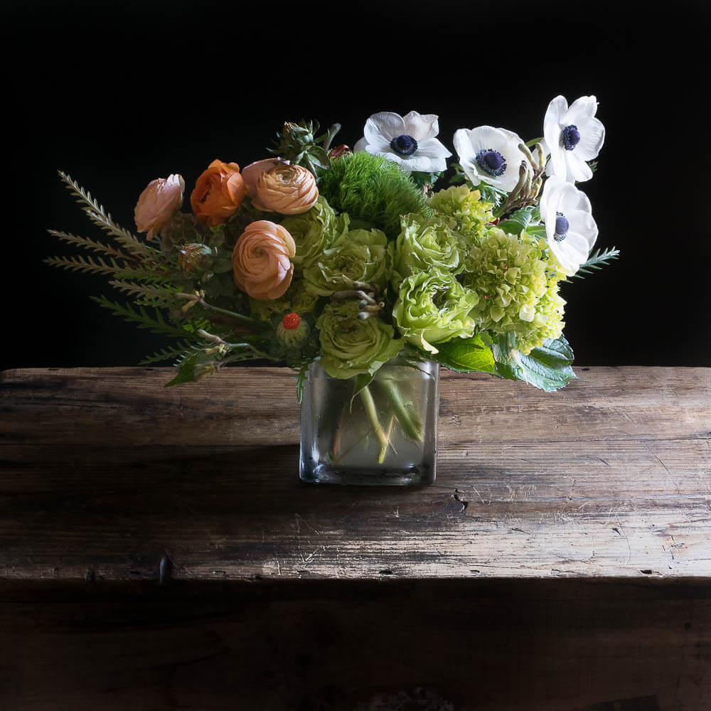 Boutique floral arrangement with orange ranunculus, white anemones, and green roses.