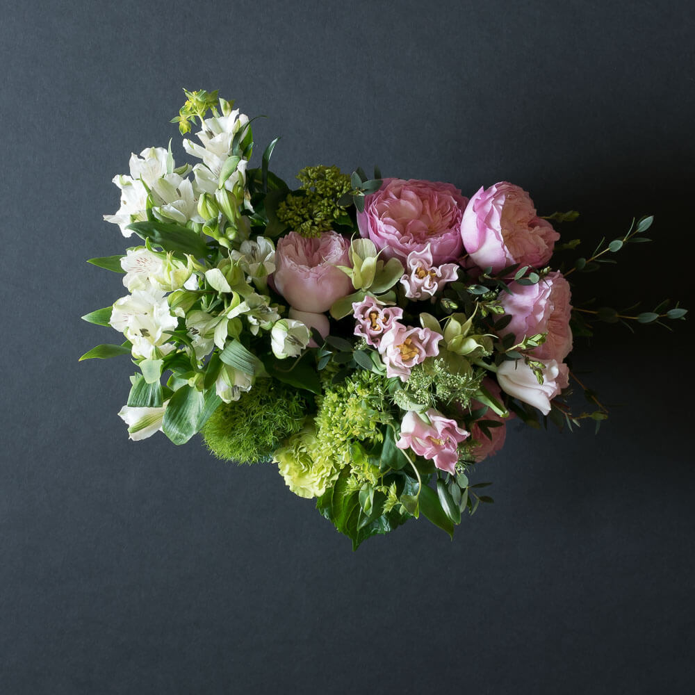 Beautiful boutique floral arrangement with light pink garden roses, light pink small roses, white alstroemerias, and mini green hydrangeas.