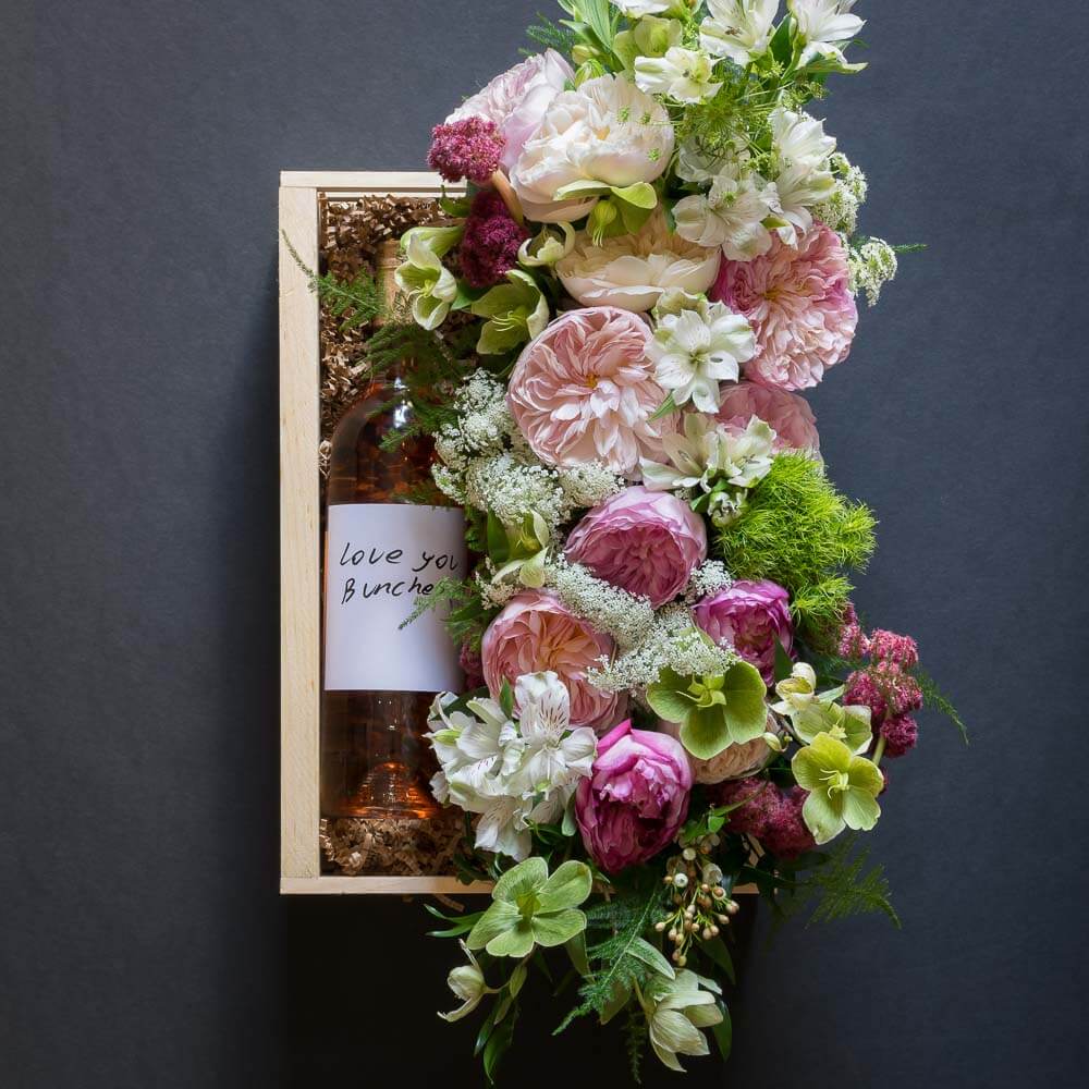 Jardin Floral gift box with light pink garden roses, light pink small roses, white alstroemerias, and mini green hydrangeas, and organic rose wine
