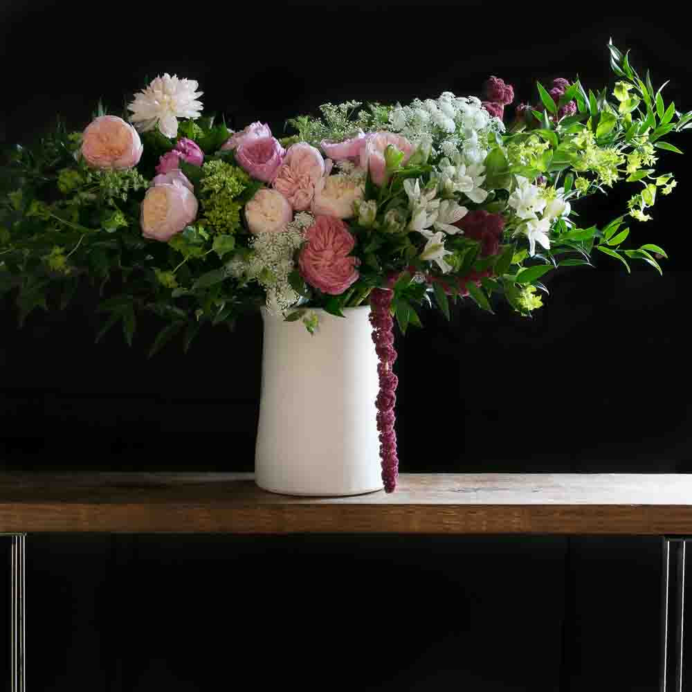 Tall beautiful boutique floral arrangement with light pink garden roses, light pink small roses, white alstroemerias, and mini green hydrangeas.