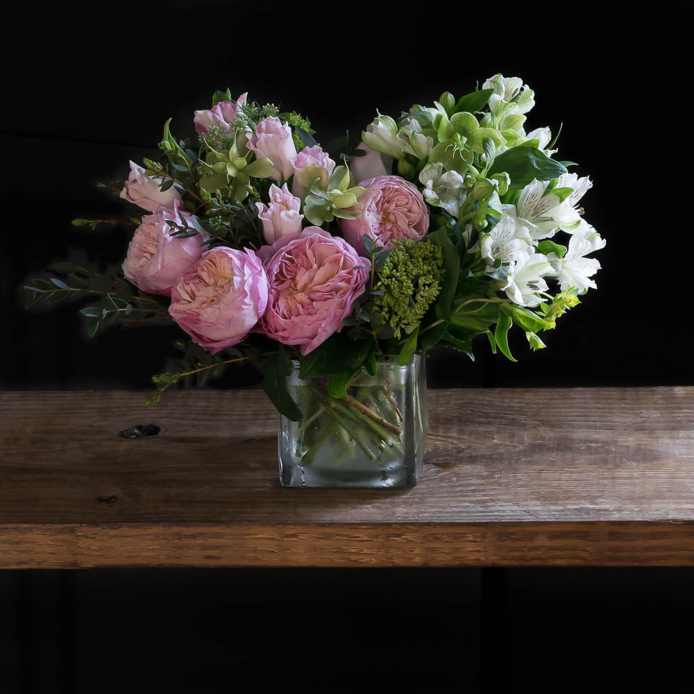 Beautiful boutique floral arrangement with light pink garden roses, light pink small roses, white alstroemerias, and mini green hydrangeas.