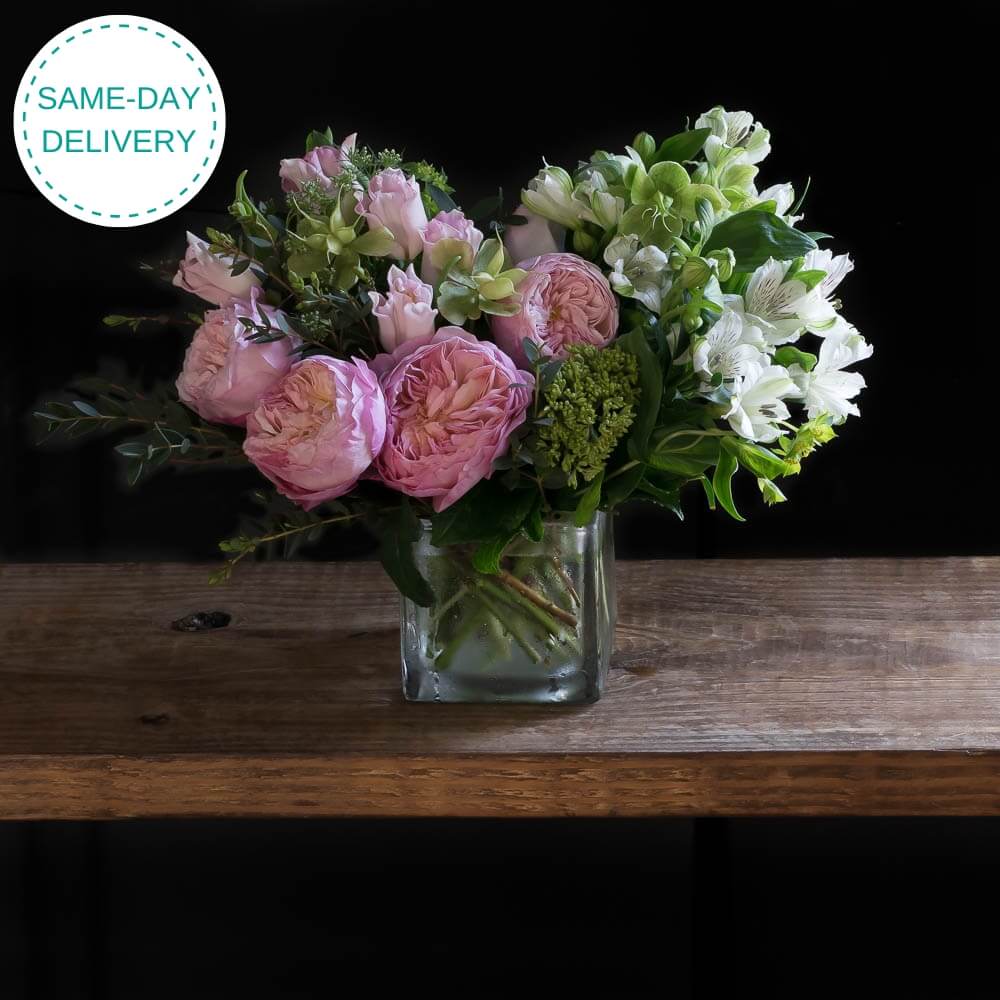 Beautiful boutique floral arrangement with light pink garden roses, light pink small roses, white alstroemerias, and mini green hydrangeas.