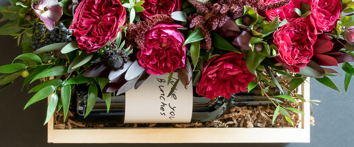 Luxe Christmas floral arrangement with red roses and wine on a box