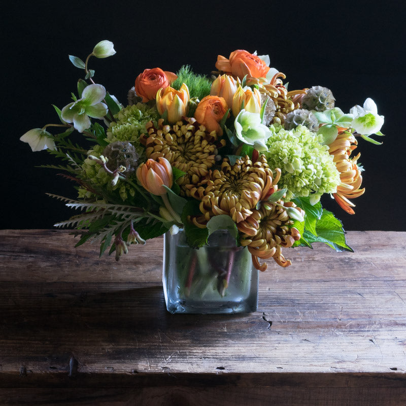 Boutique fall floral arrangement with orange roses, orange ranunculus and tulips.