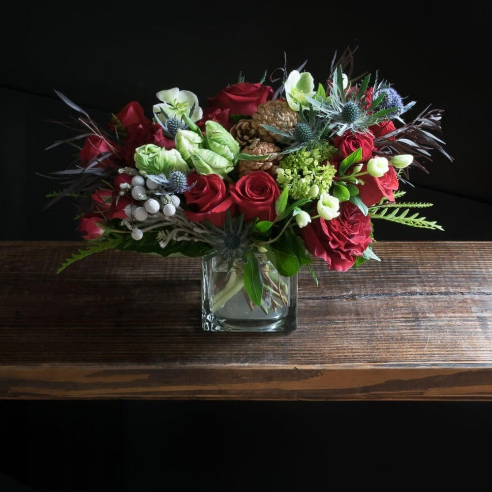 Unique Holiday Christmas floral arrangement of red rose, white parrot tulips, and cones.