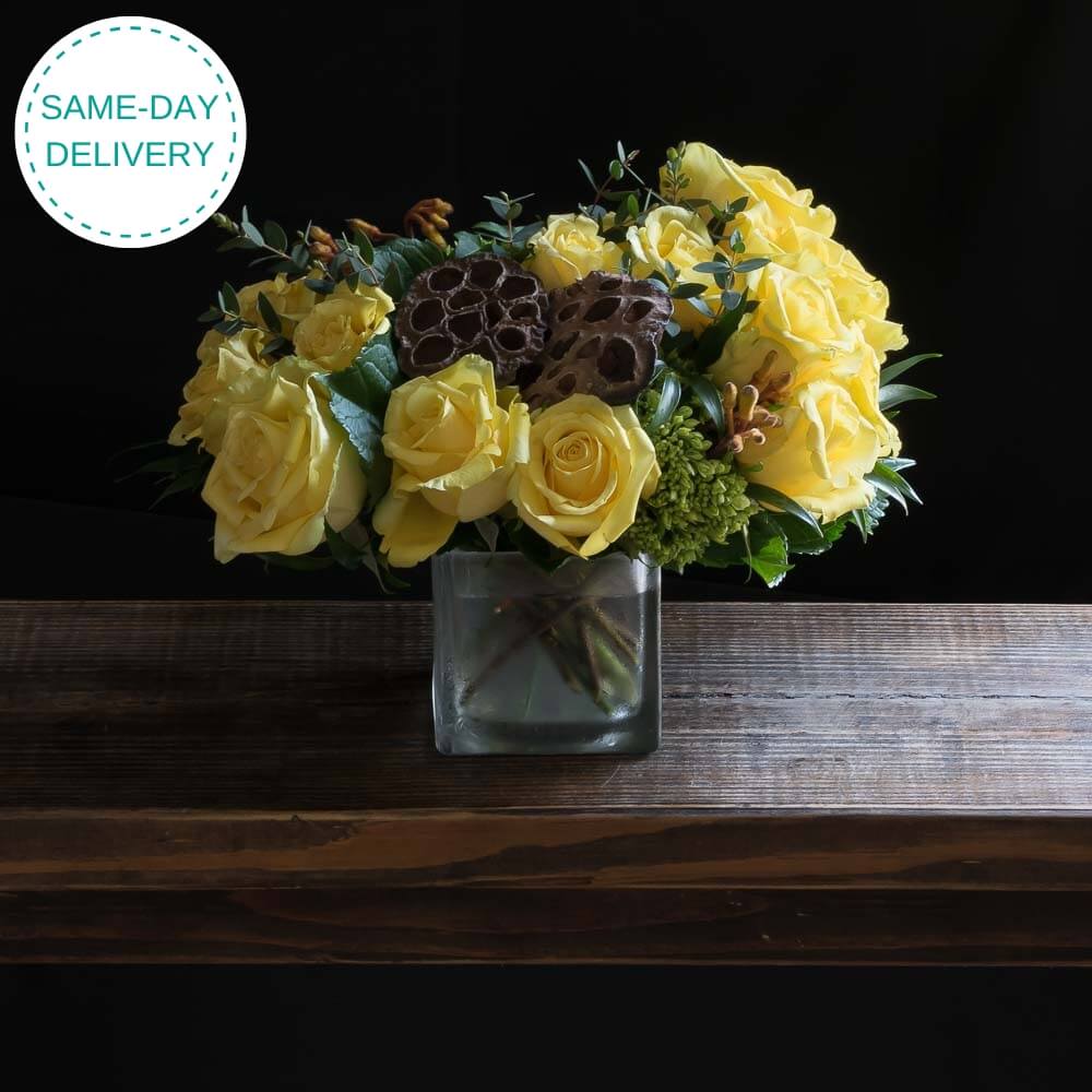 Bouquet of yellow roses in a clear vase on a wooden surface with 'Same-Day Delivery' text.