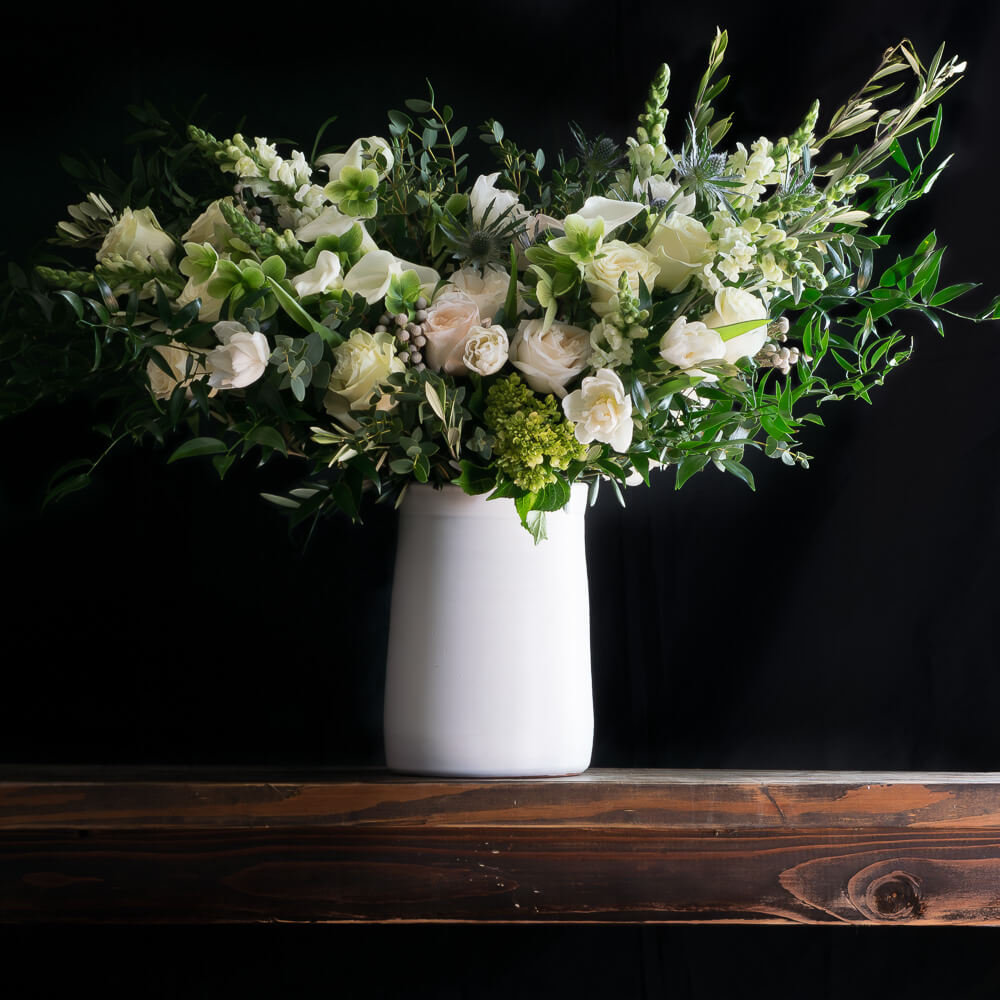 Tall boutique floral arrangement with white tulips, white roses, white calla lilies, and green mini hydrangeas