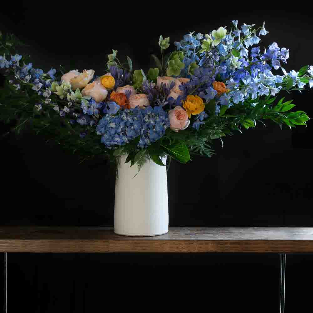 Boutique tall floral arrangement with blush roses, blue flowers, hellebores, hydrangeas