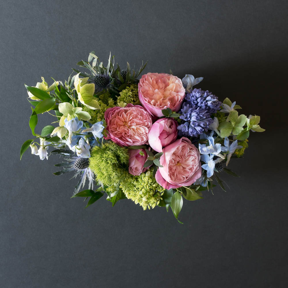 Unique floral arrangement with light pink David Austin garden roses, light pink small roses, blue hyacinths, and mini green hydrangeas, from the top