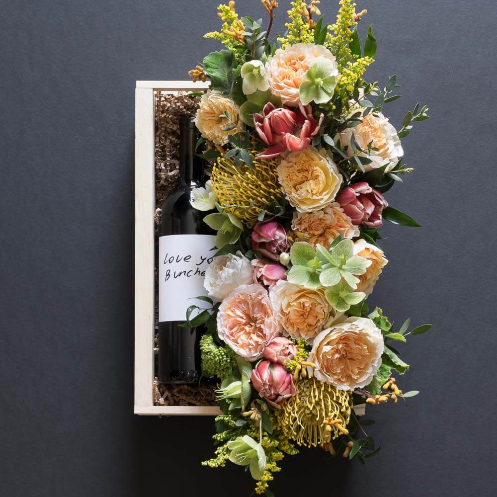 Jardin floral gift box with blush roses, red tulips, hellebores, hydrangeas, and yellow balls, with organic red wine