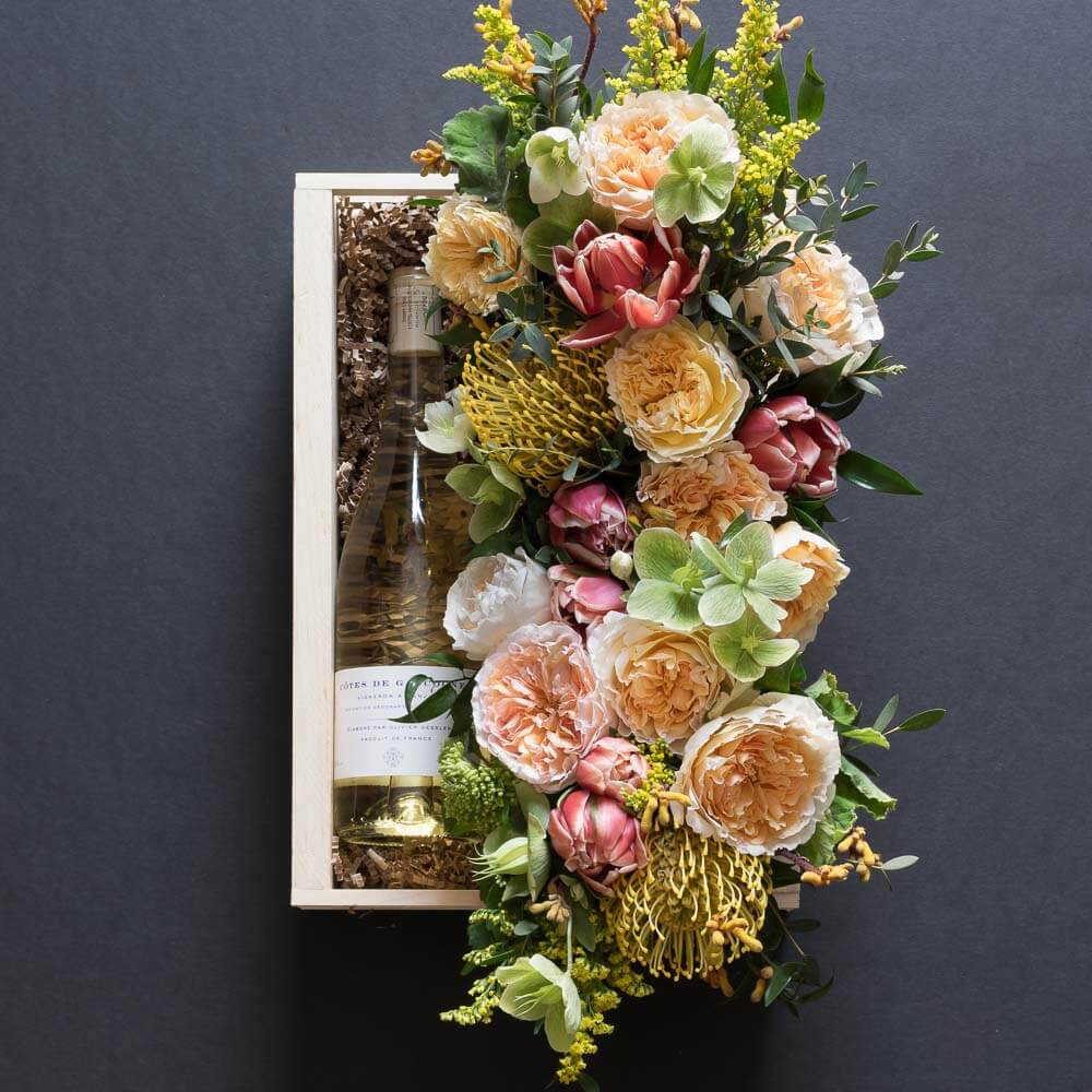 Beautiful floral arrangement with blush roses, red tulips, hellebores, hydrangeas, and yellow balls, with organic white wine