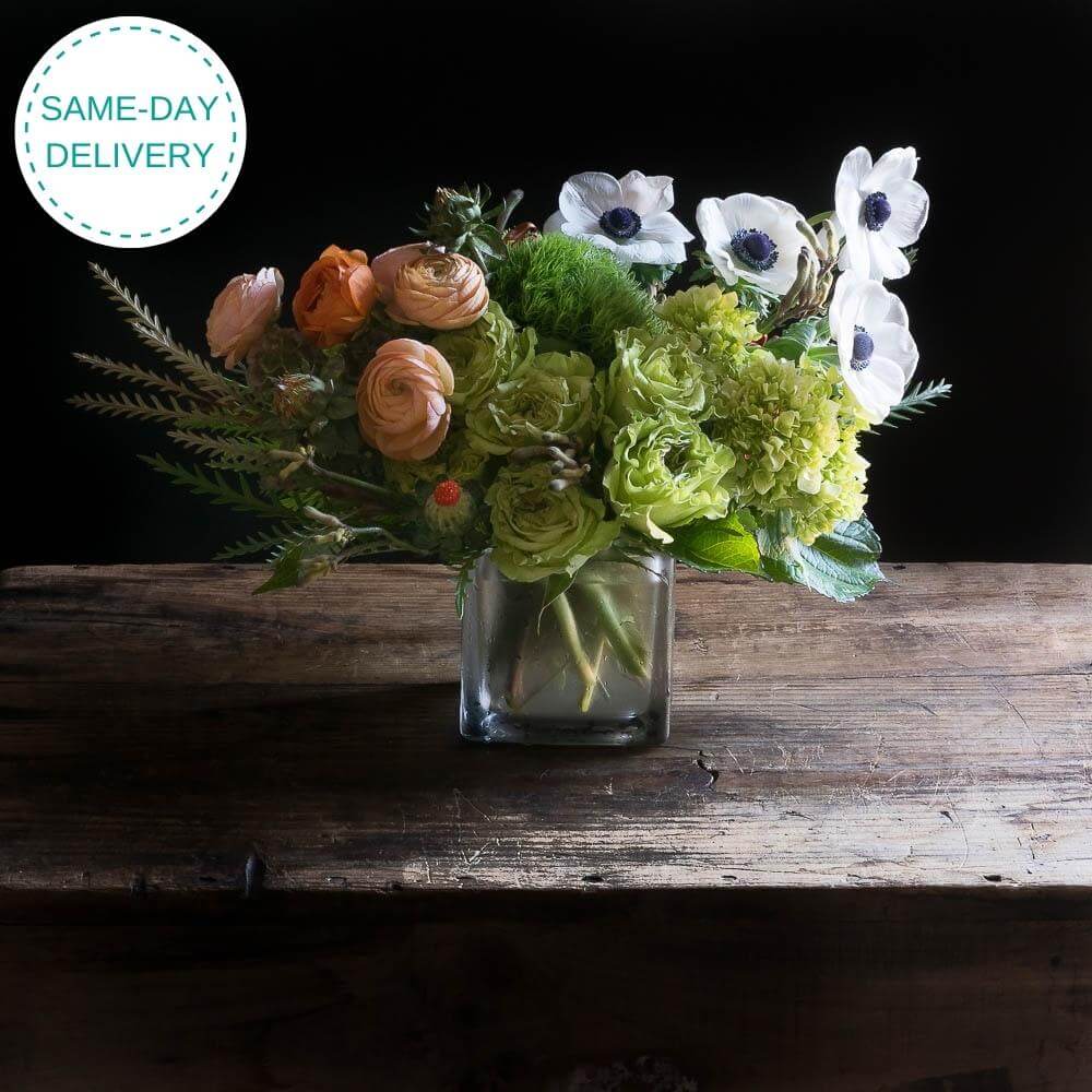 Beautiful boutique fall floral arrangement with orange roses, light orange ranunculus, green roses, and white anemones.