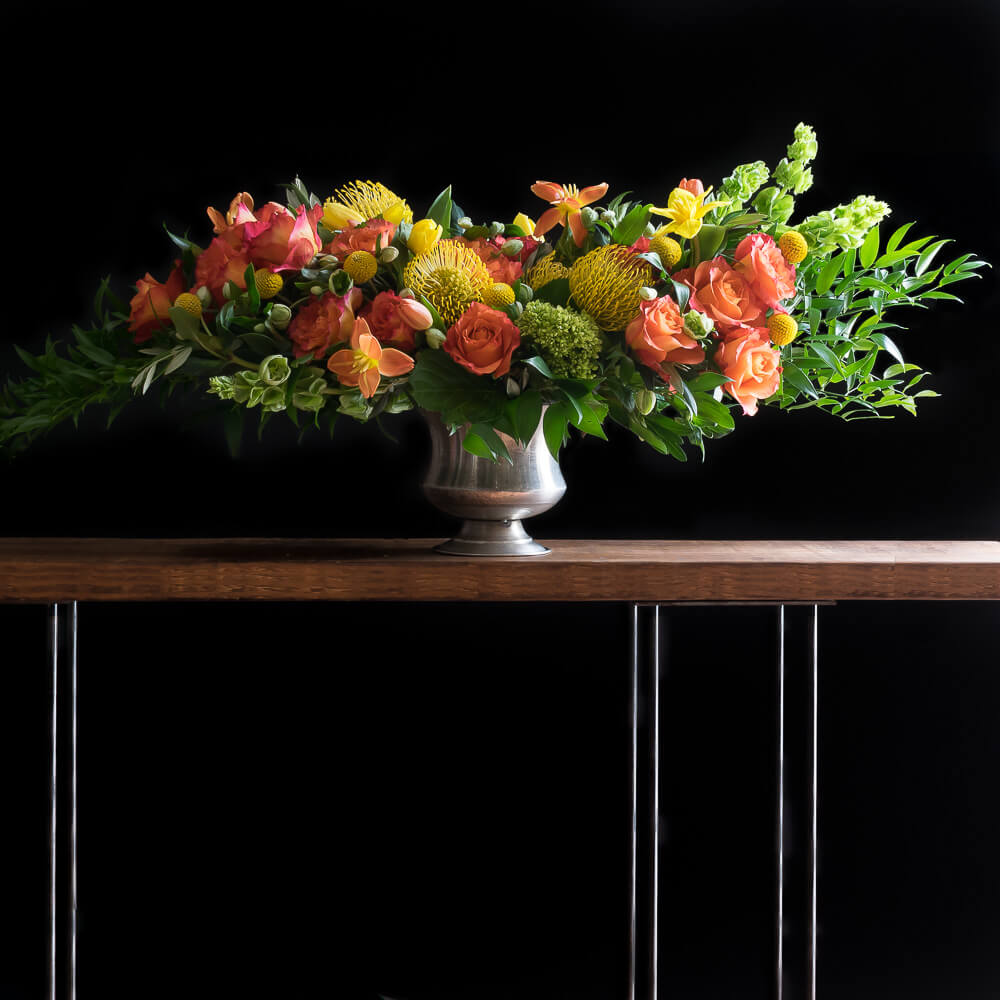 Luxe boutique floral arrangement with orange roses and yellow flower, and mini green hydrangeas