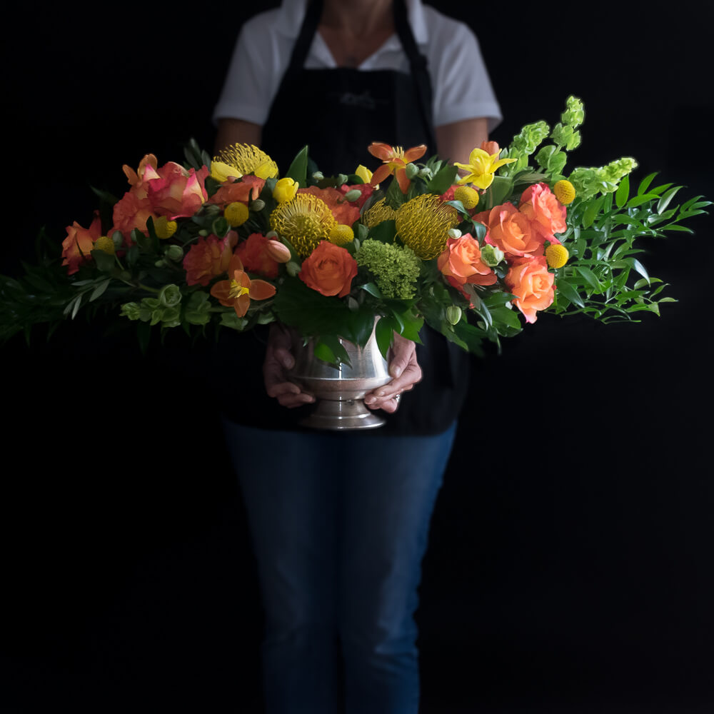 Luxe boutique floral arrangement with orange roses and yellow flower, and mini green hydrangeas