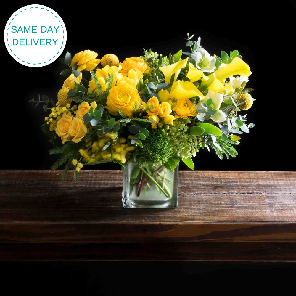 Beautiful boutique flower arrangement - yellow ranunculus, yellow calla lilies, light yellow spray roses, and mini green hydrangeas.