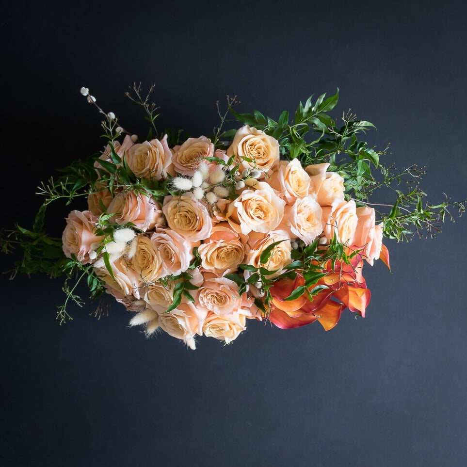 Unique boutique floral arrangement with peach roses and calla lilies