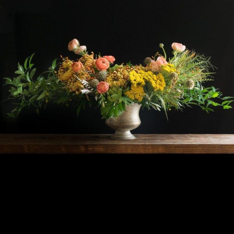 Beatiful boutique fall floral arrangement with orange, yellow flowers, and light orange ranunculus.