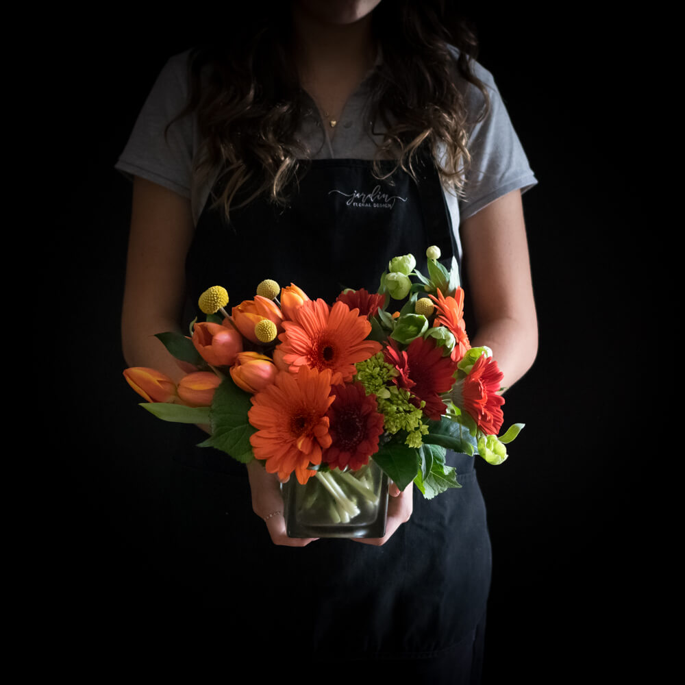 Floral arrangement with orange tulips, orange gerberas, red gerberas, and mini green hydrangeas.